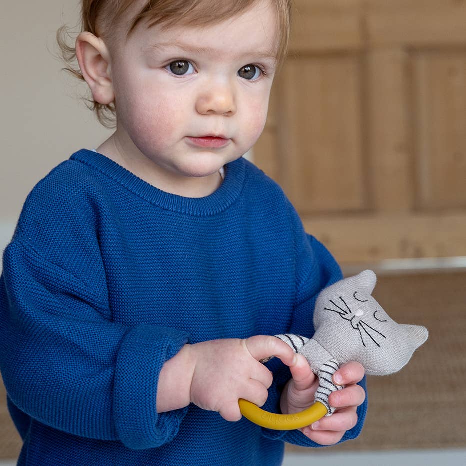 Child in a blue sweater holding a toy with a cat design and a yellow ring.