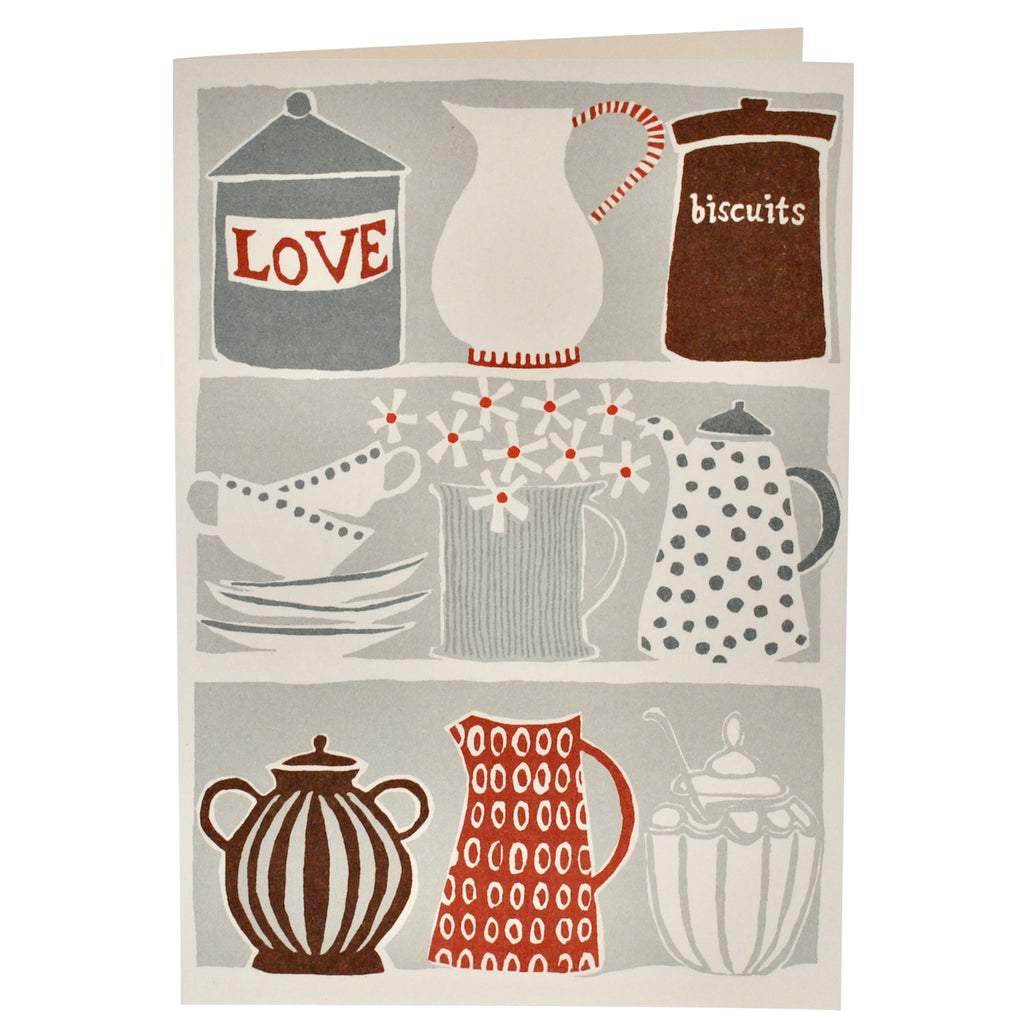 Grey greetings card, with shelves stacked with jugs, teapots and biscuit tins. Designed by CAMBRIDGE IMPRINT