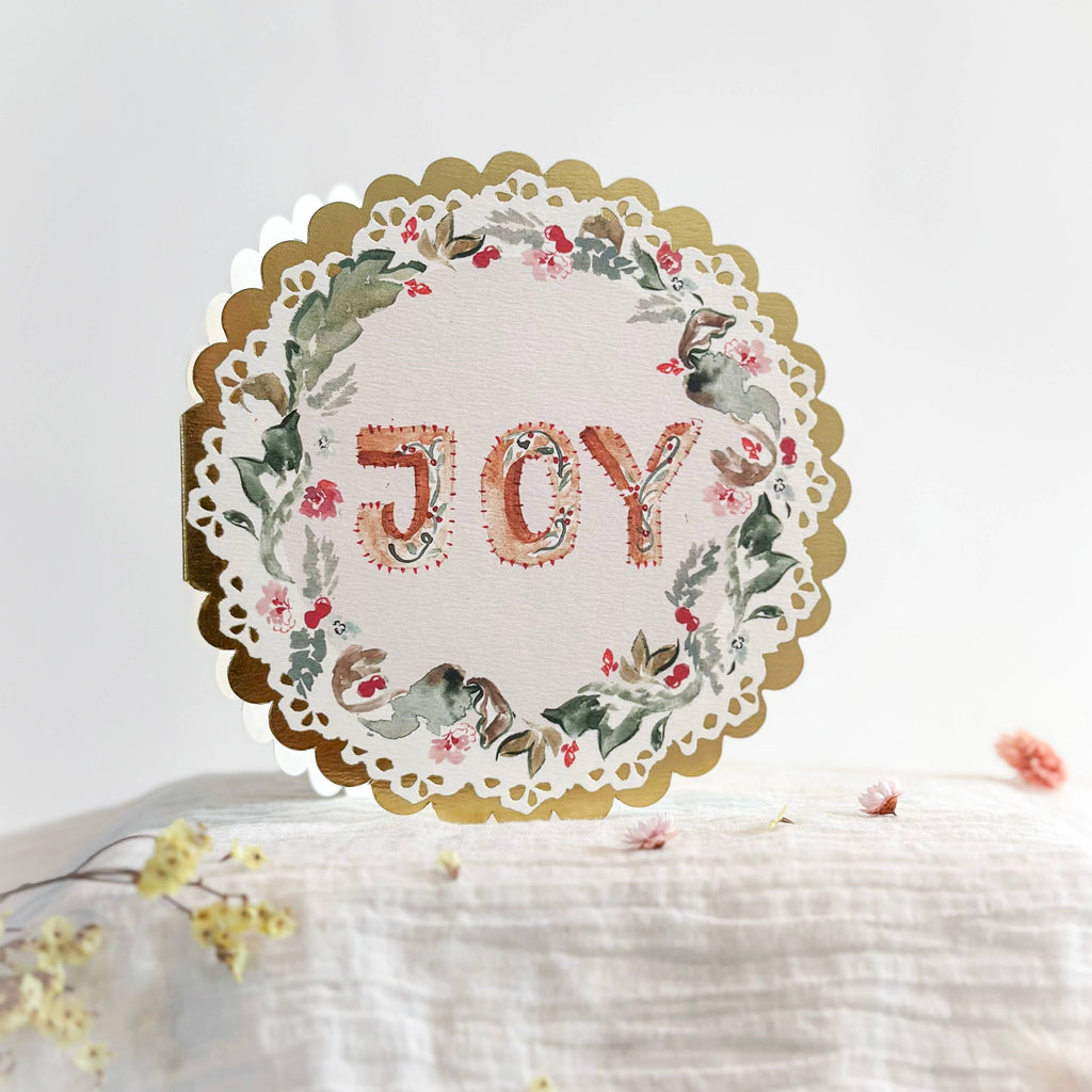 circular christmas card with gold foil edge and message that reads 'joy'