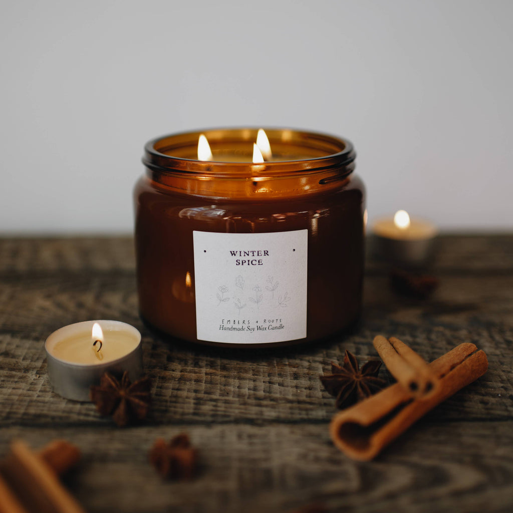 Candle in an amber jar with a label, surrounded by cinnamon sticks and star anise on a textured surface.