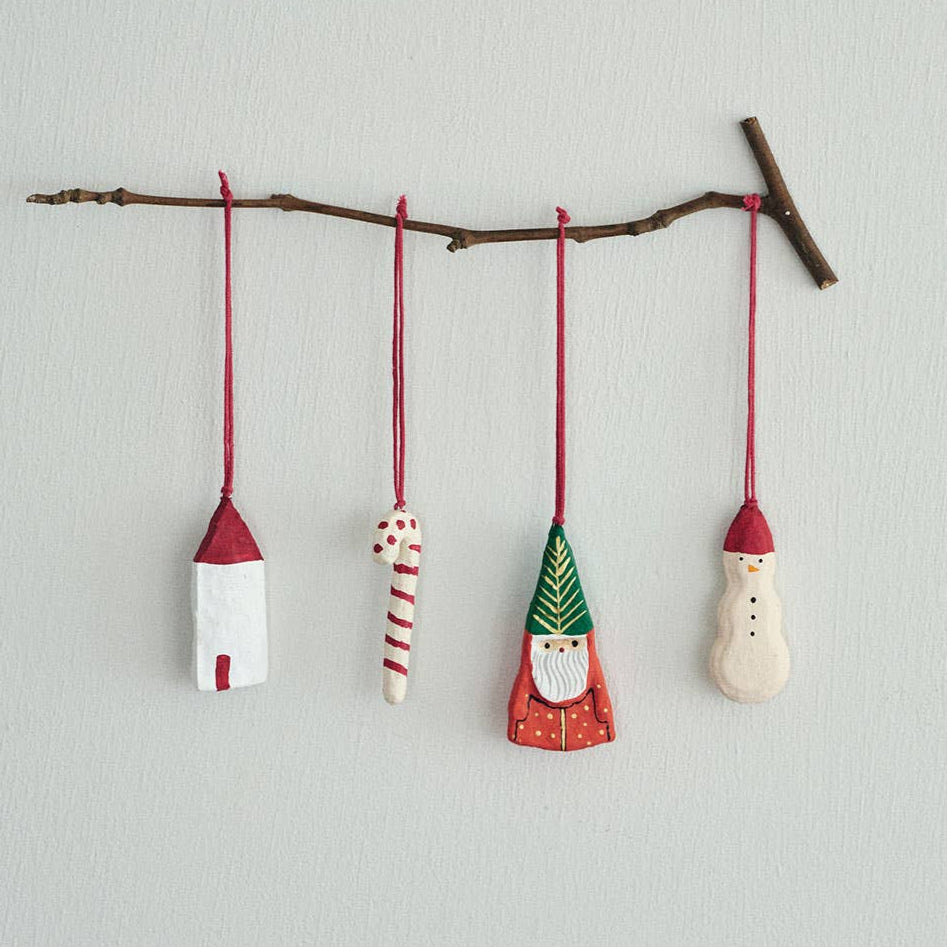 Decorative paper mache Christmas ornaments hanging from a branch on a light gray background