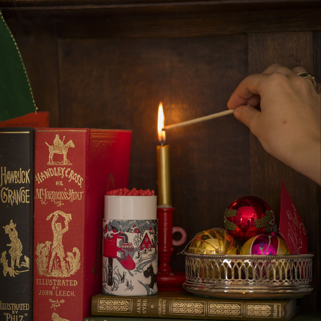 Person lighting a candle on a shelf with books and decorative items