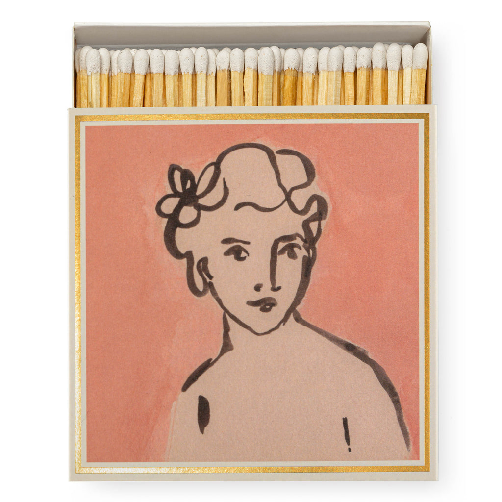 Boxed matches by Wanderlust Paper Co, featuring a vintage-style portrait illustration of a seated figure, on a pink background and gold-foiled edge.