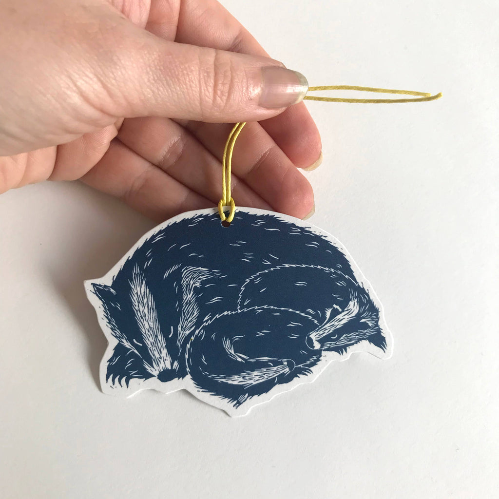 Hand holding a blue and white decorative ornament with a badger design on a light background