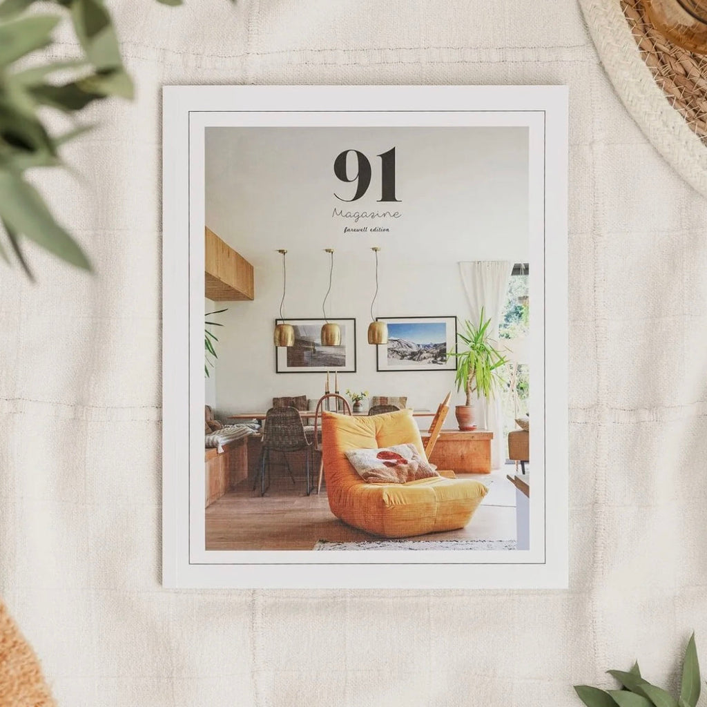 91 magazine, on a cream tablebloth with green foliage surrounding