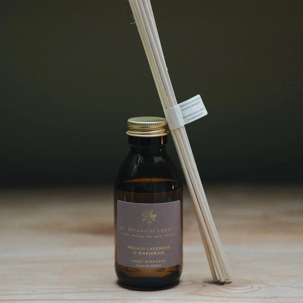 A scented reed diffuser in an amber bottle with a soft purple label., blended with French lavender and Marjoram, and with 8 rattan reeds. Made by Botanical Candle Co.