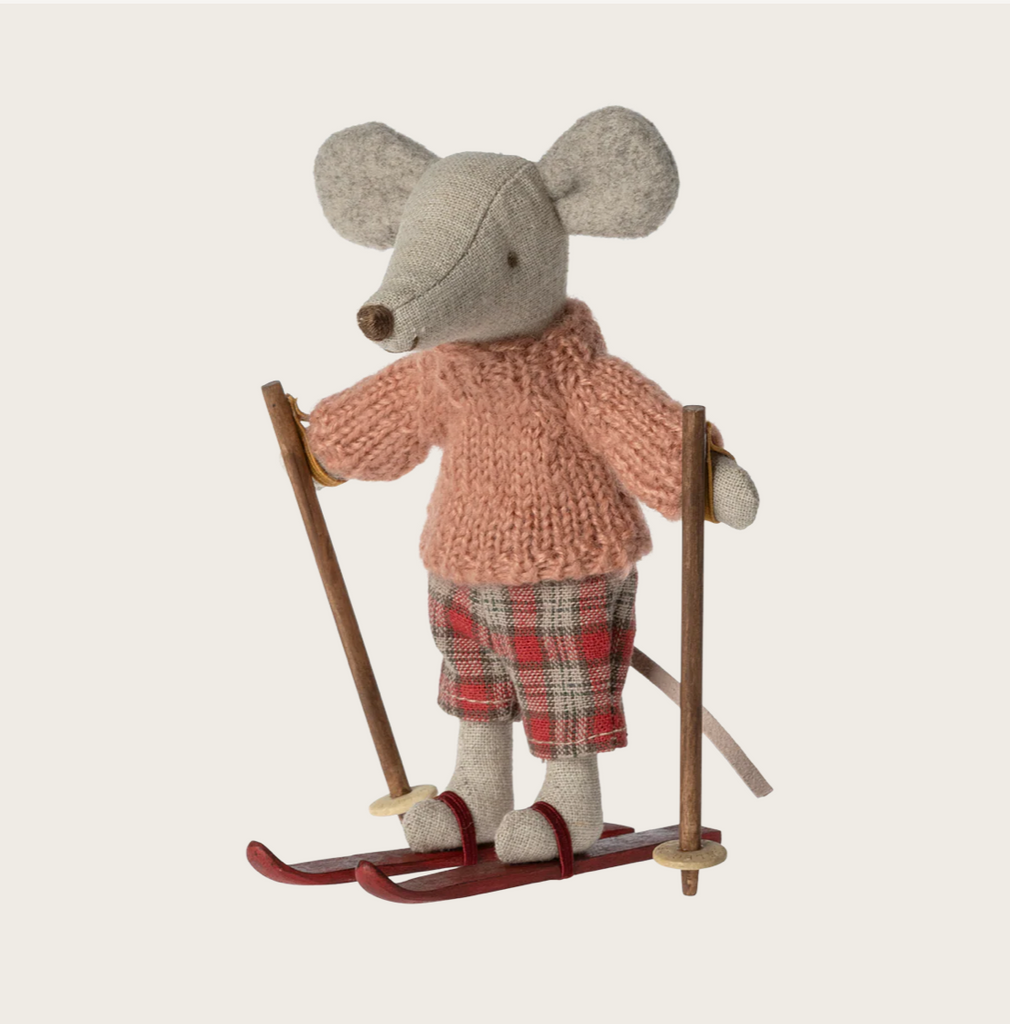Stuffed mouse toy in a sweater and plaid pants standing on skis with ski poles against a light background