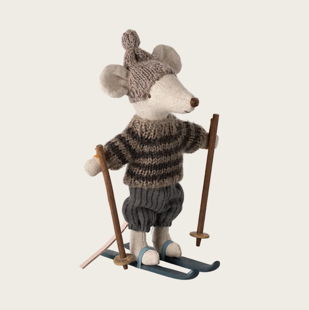 Stuffed toy mouse in winter attire with skis and ski poles on a light background