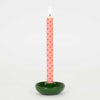 Pink polka dot candle in a green holder on a white background