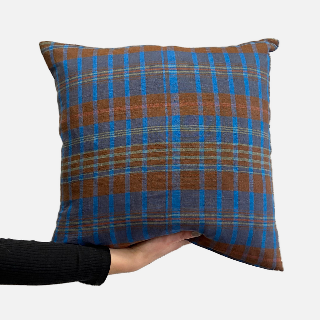 Plaid blue & brown cushion held by person in front of white background