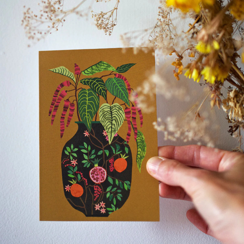 Hand holding a card with a colorful plant illustration against a neutral background