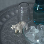 Small polar bear christmas decoration on a textured surface with a clear glass and blue container in the background.