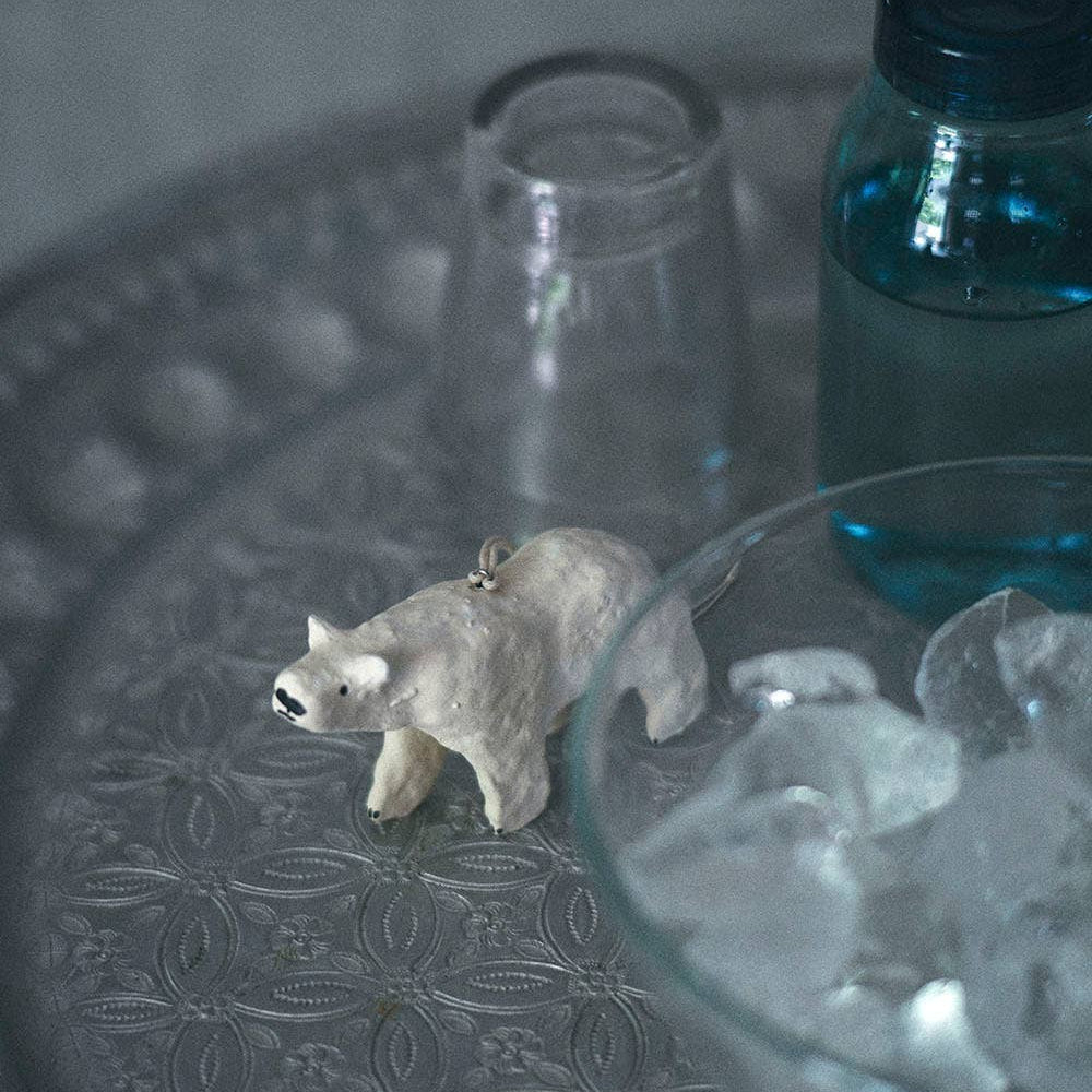 Small polar bear christmas decoration on a textured surface with a clear glass and blue container in the background.
