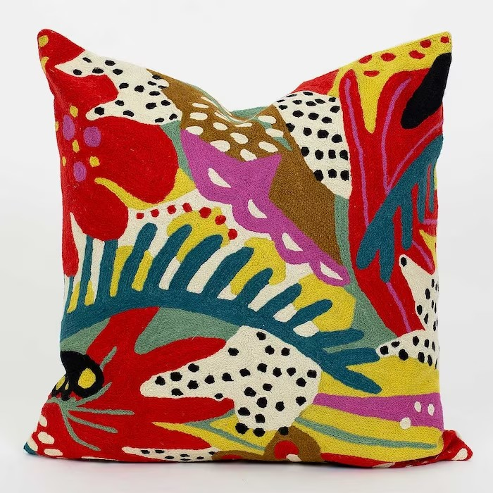 Colourful handmade bed or sofa cushion with red, yellow, blue and pink stitching and dots covering.